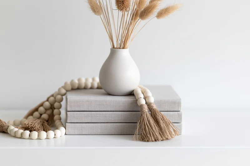 White ceramic vase with dried bunny tail grass stems on stack of linen-covered books on white shelf