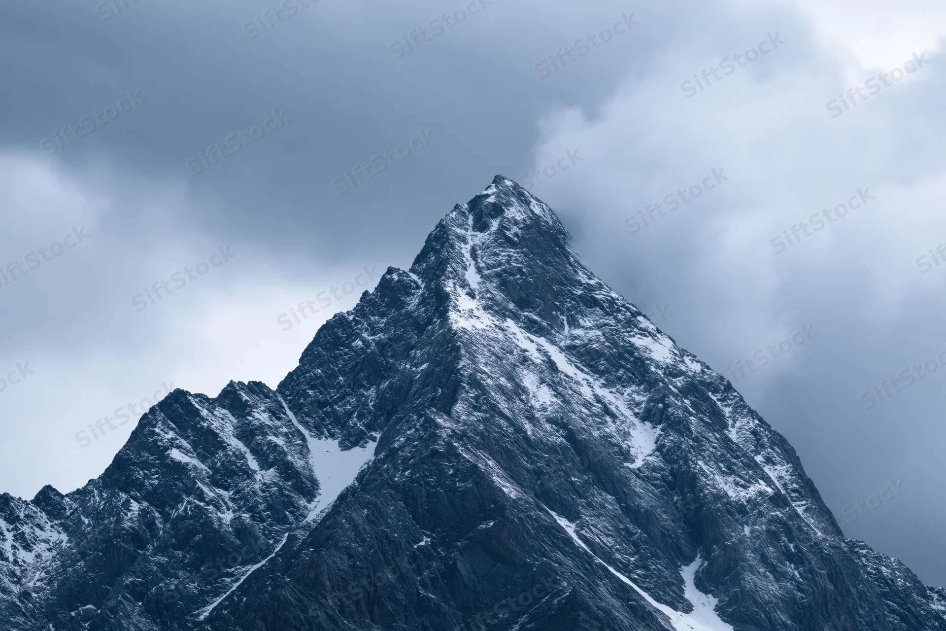 Snow-dusted rocky mountain peak under cloudy sky