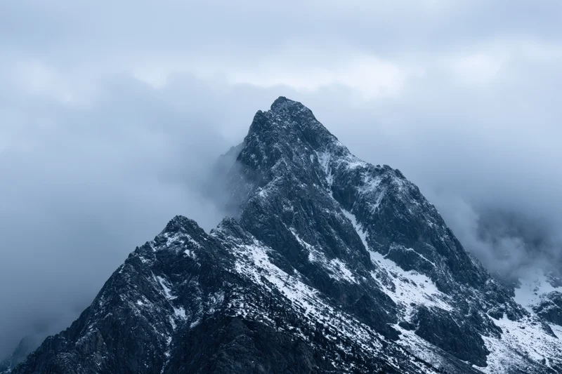 Snow-dusted rocky mountain peak emerging from dense clouds