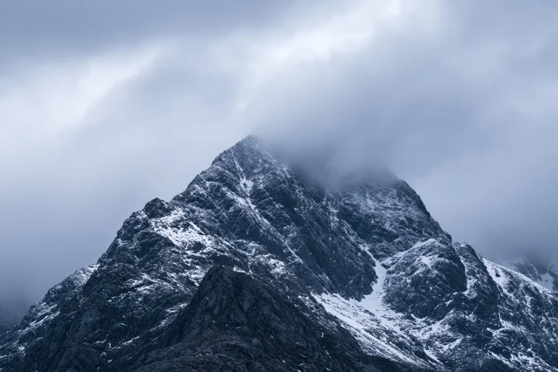 Snow-dusted rocky mountain peak partially covered by dense clouds