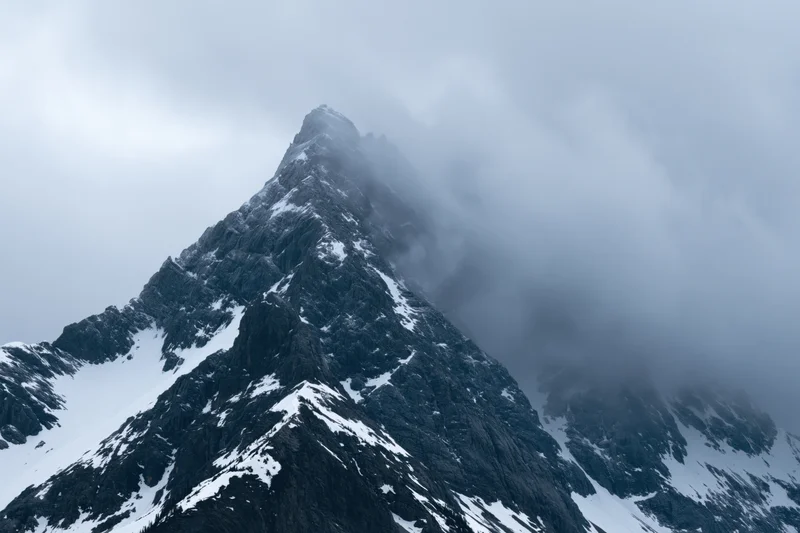 Snow-dusted rocky mountain peak partially obscured by dense clouds