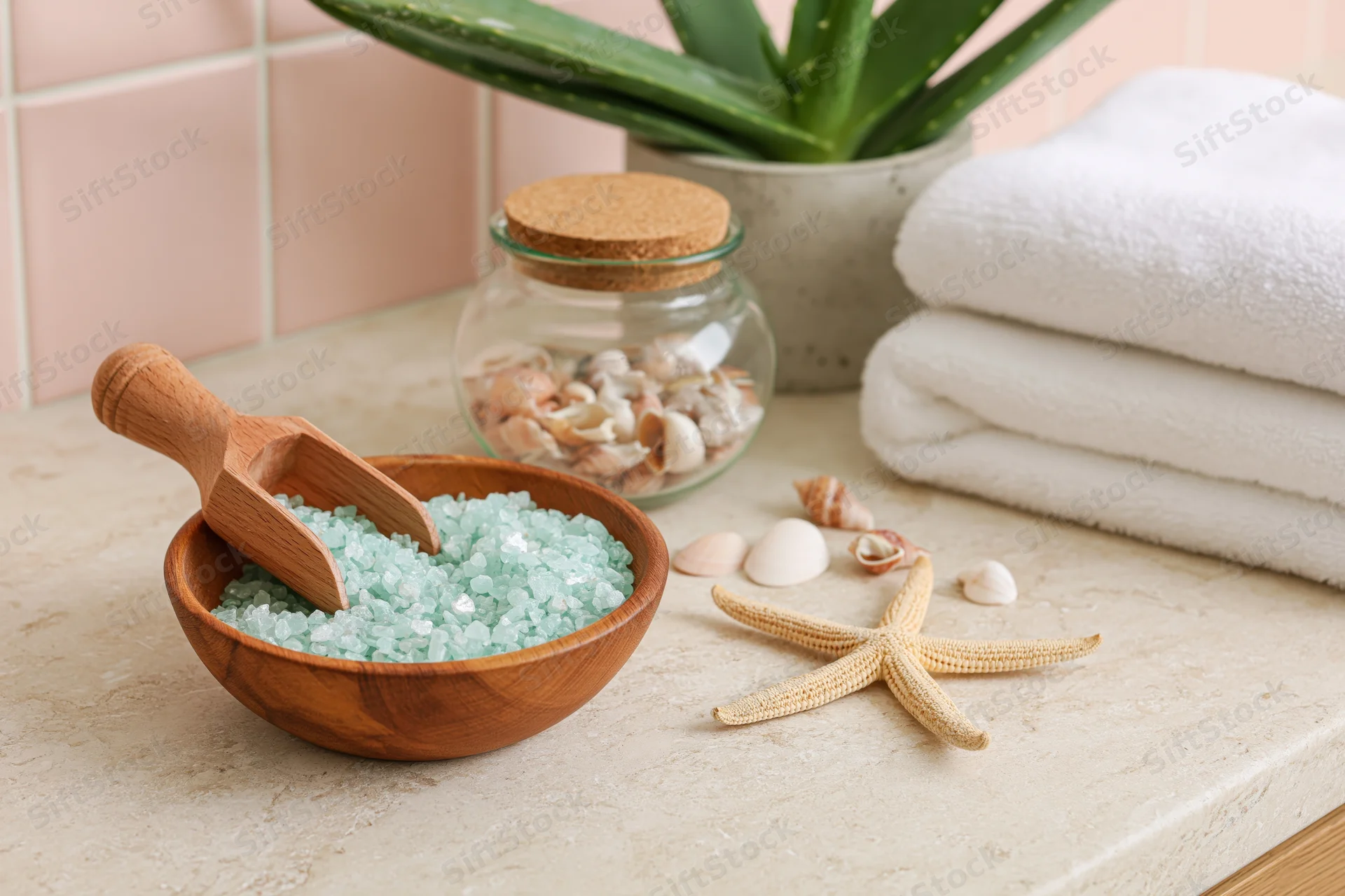 Bath salt in a wooden bowl with seashells and aloe on a stone countertop
