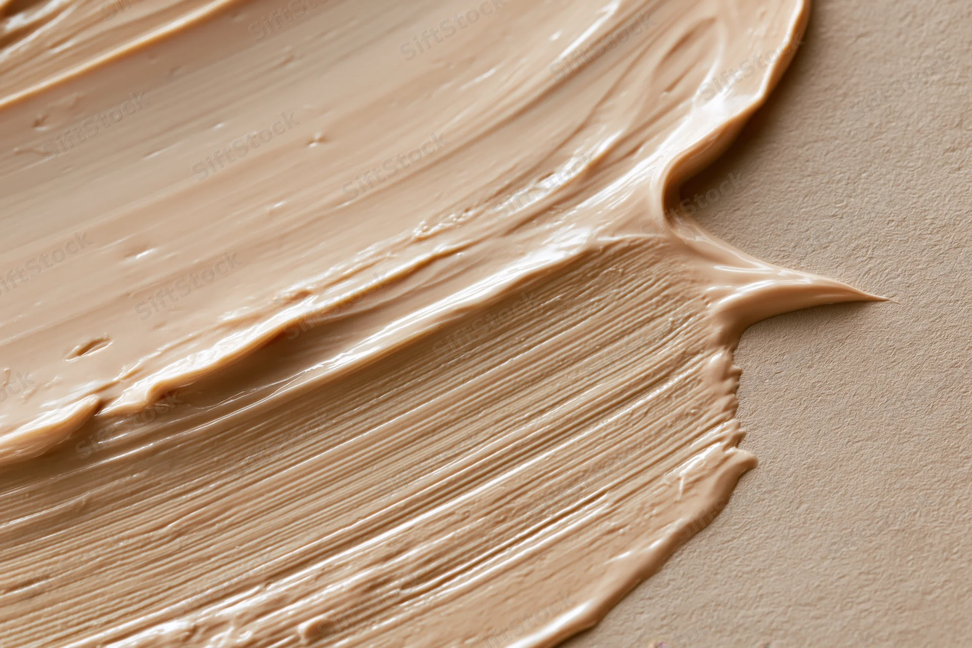Thick creamy beige cosmetic foundation smeared across a flat surface with visible texture and blend marks