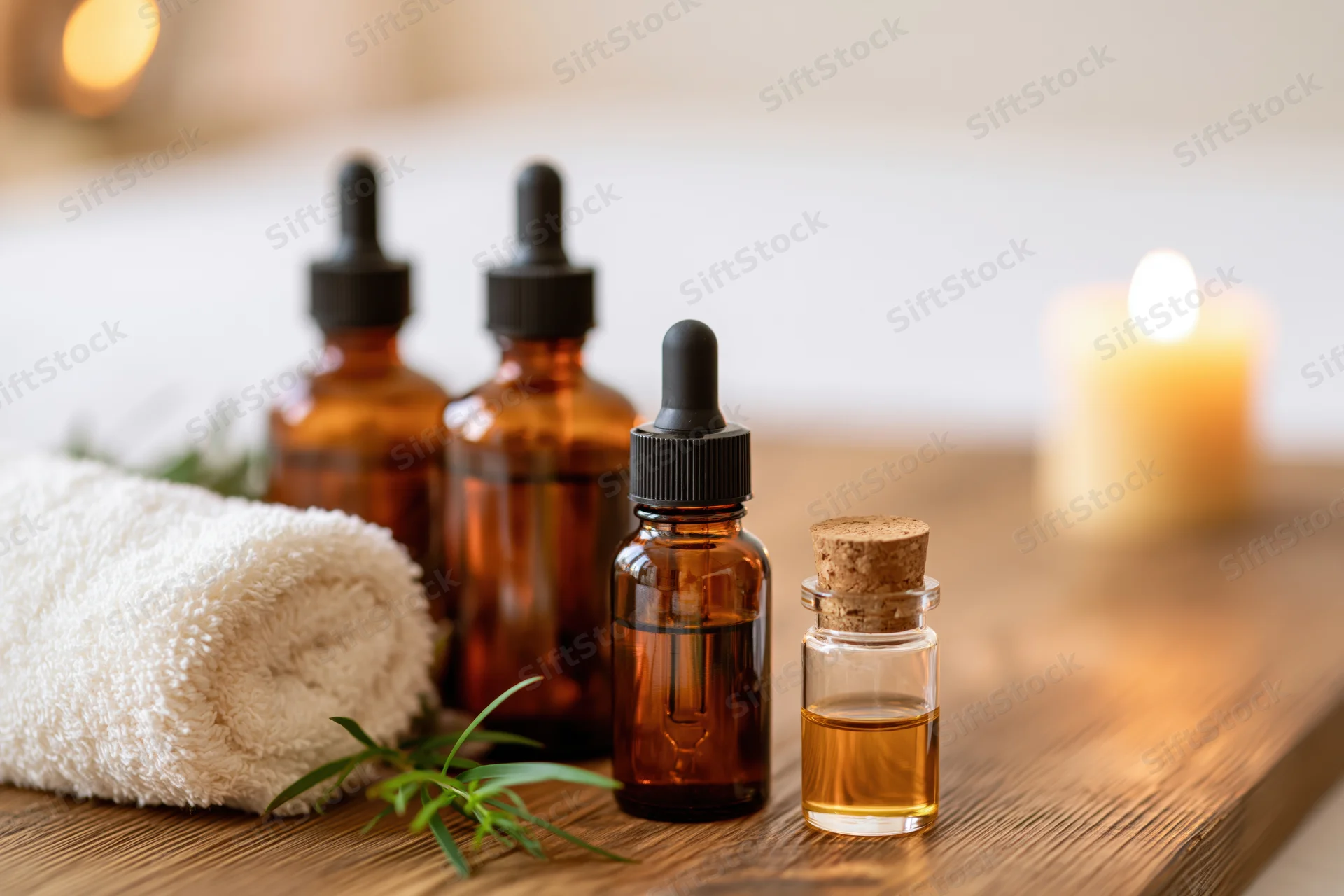 Essential oil bottles with towel and candle on wooden table