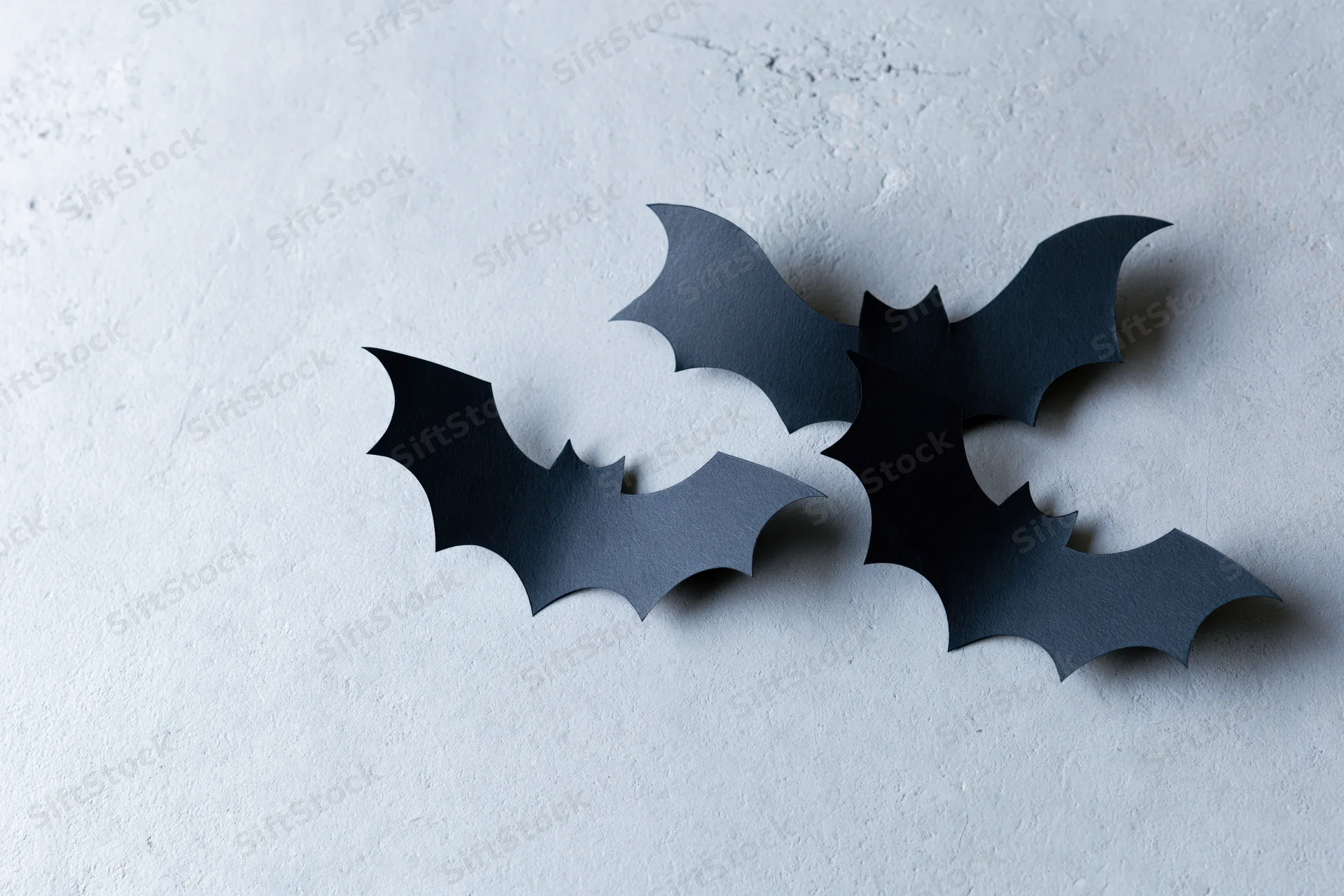 Three black paper bat cutouts arranged in a loose flying cluster on a textured gray surface