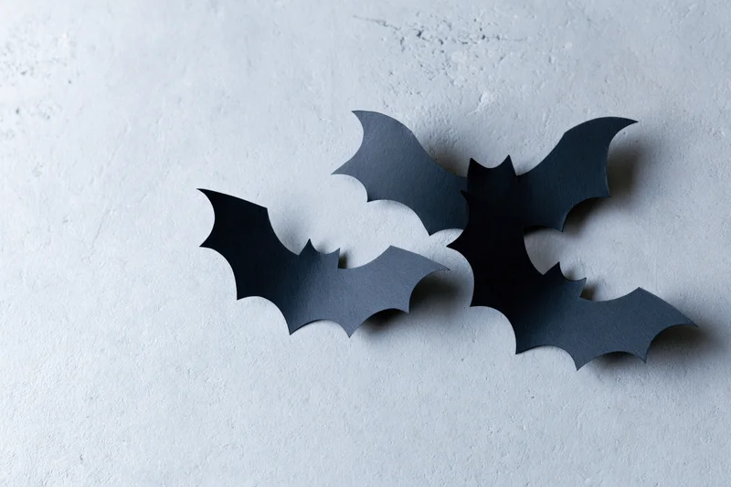 Three black paper bat cutouts arranged in a loose flying cluster on a textured gray surface