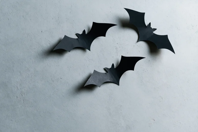 Three black paper bat cutouts arranged in a loose flying cluster on a textured gray wall