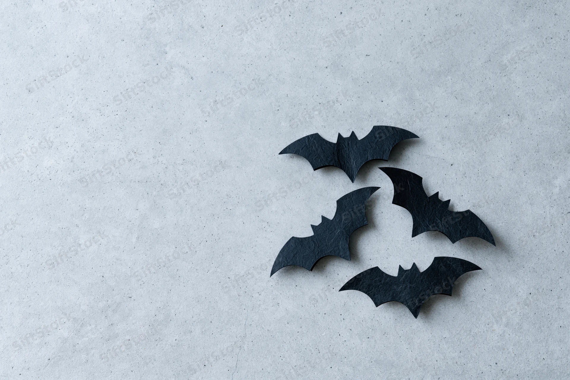 Four black paper bat cutouts arranged in a loose cluster on a textured gray surface