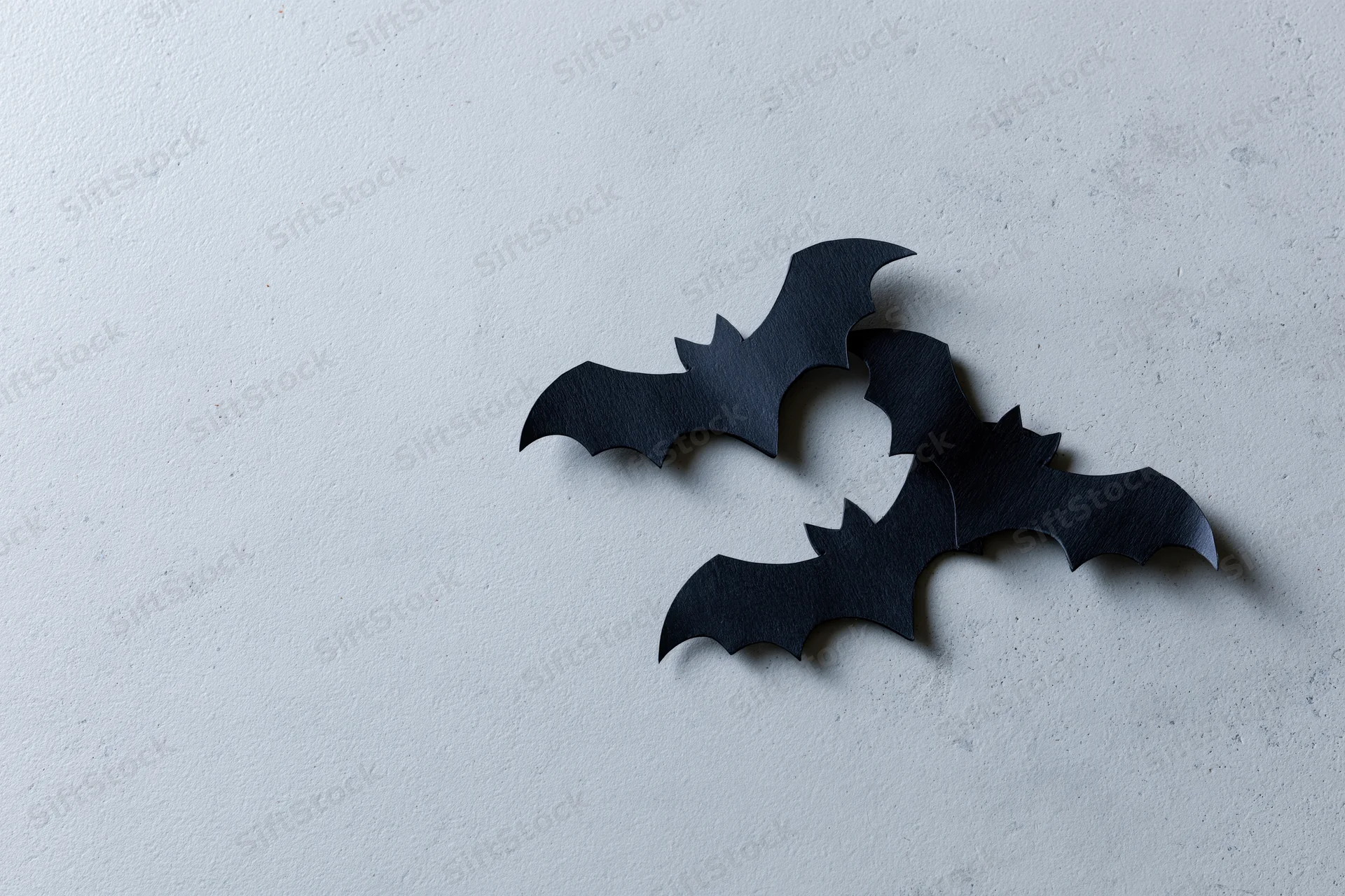 Three black paper bat cutouts arranged in a loose flying cluster on a white textured surface
