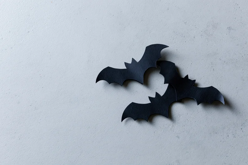 Three black paper bat cutouts arranged in a loose flying cluster on a white textured surface
