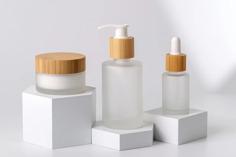 Three frosted glass skincare bottles with bamboo caps on white pedestals
