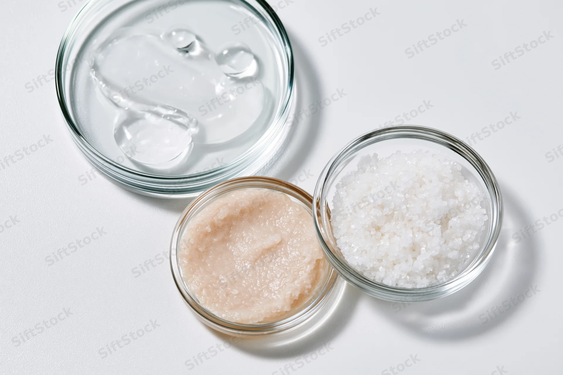 Three glass petri dishes containing different skincare ingredients arranged on a white surface