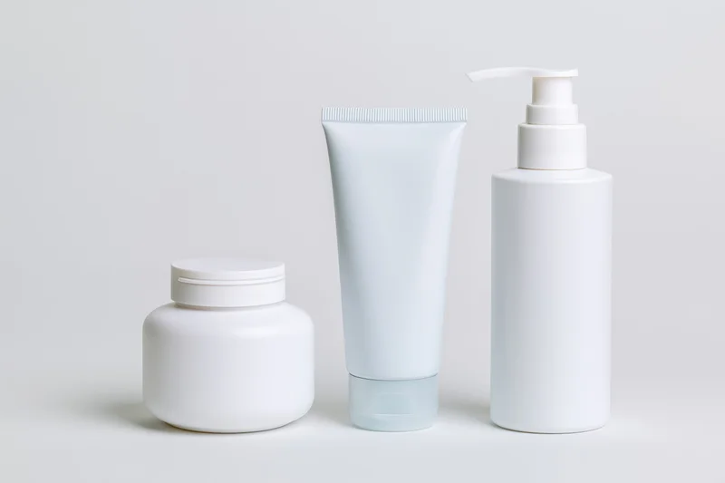 Three white unlabeled skincare containers arranged in a row on a plain white surface