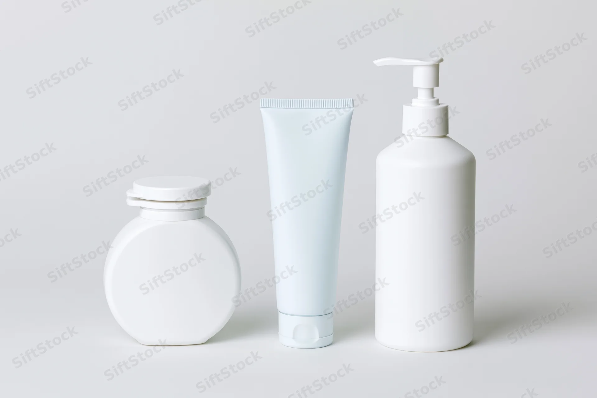 Three white unlabeled skincare containers arranged in a row on a plain white surface