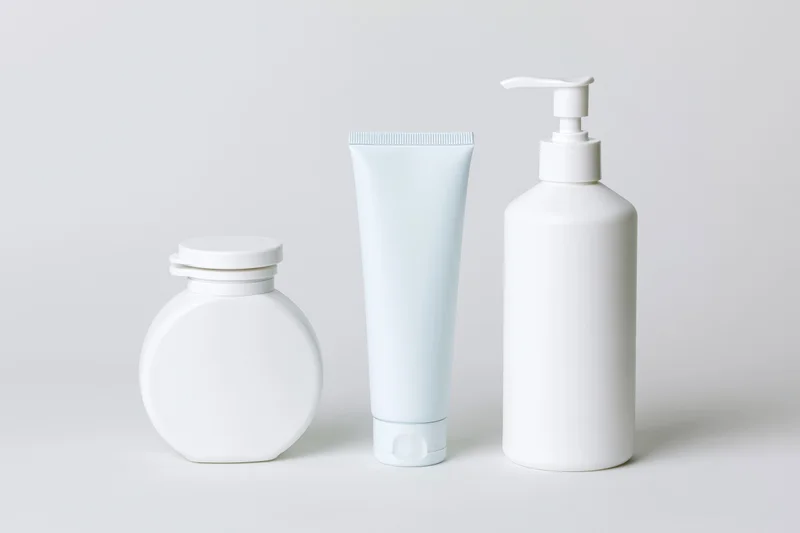 Three white unlabeled skincare containers arranged in a row on a plain white surface