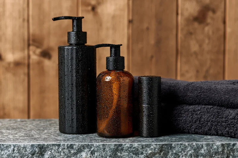 Three wet grooming bottles on a grey stone countertop with a dark towel and wooden background