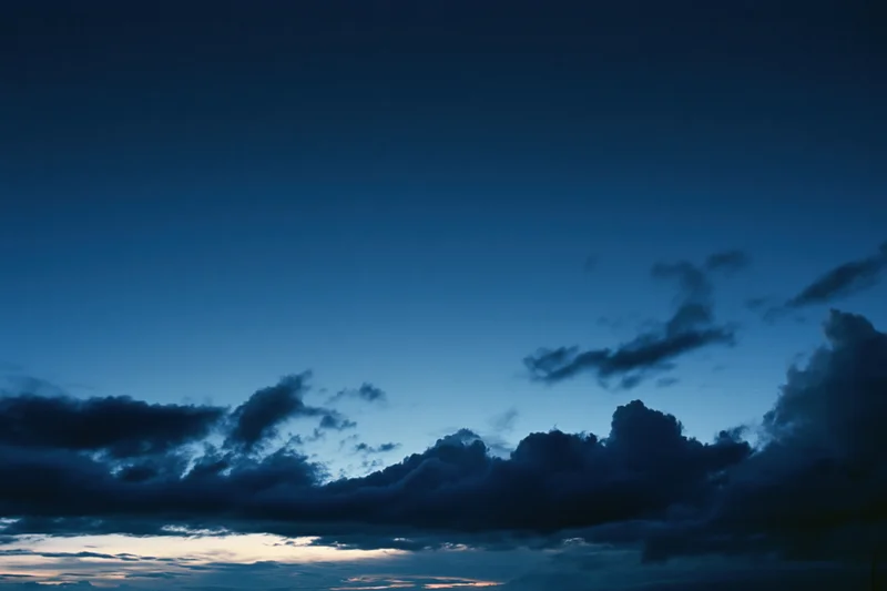 Twilight sky with scattered dark storm clouds above a fading horizon