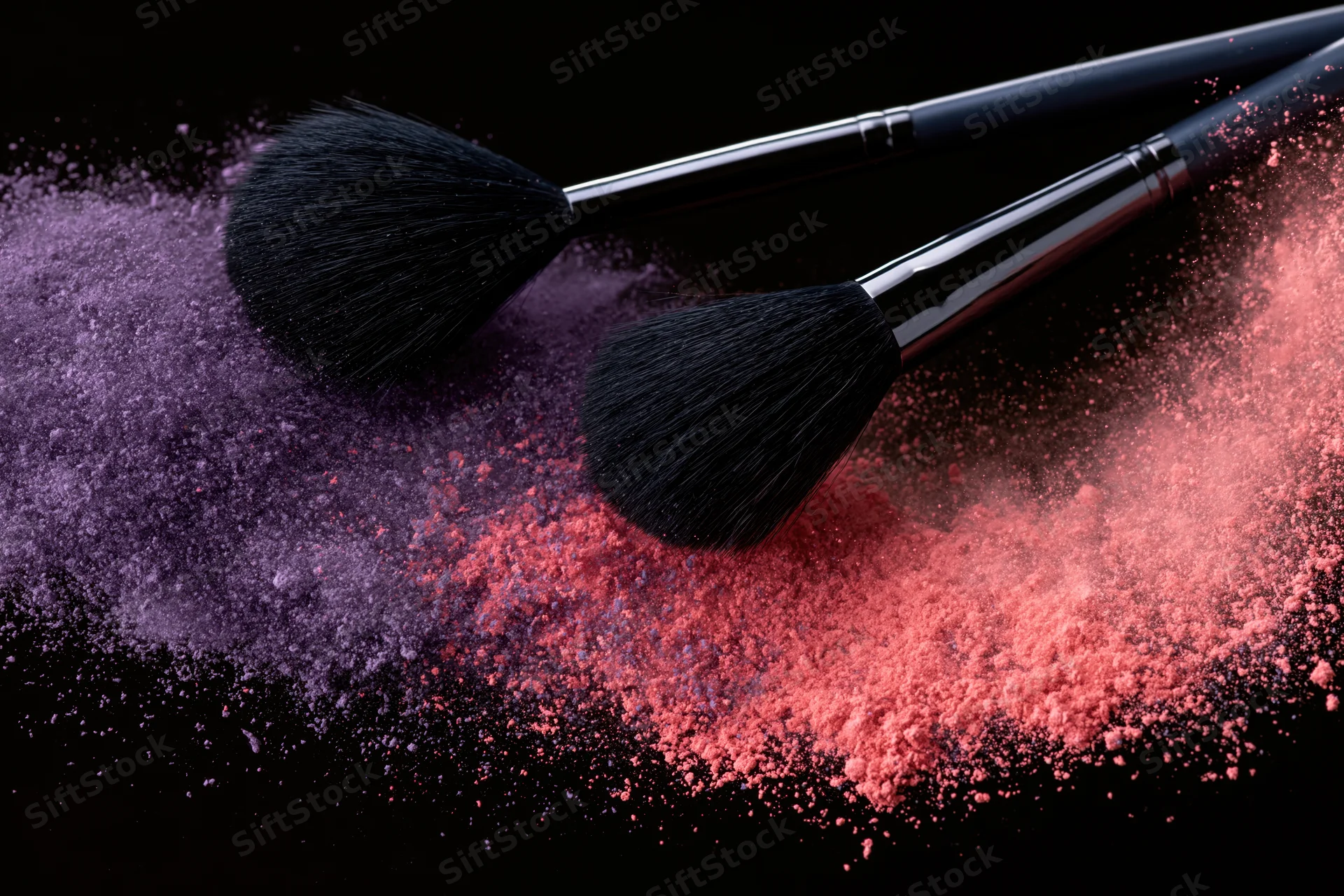 Two black makeup brushes mid-swipe releasing purple and pink powder against black background