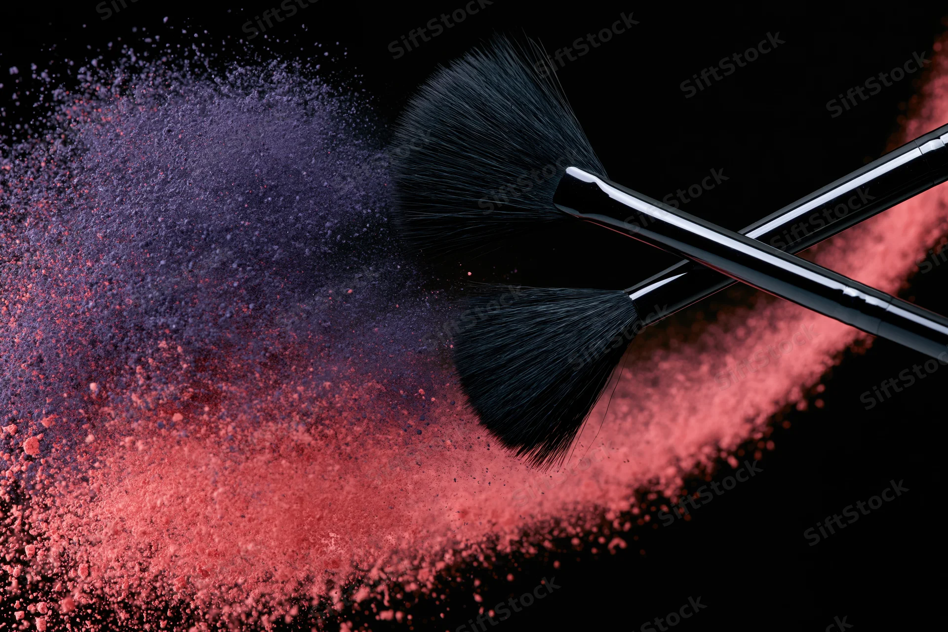 Two black makeup brushes mid-swipe releasing red and purple powder against black background
