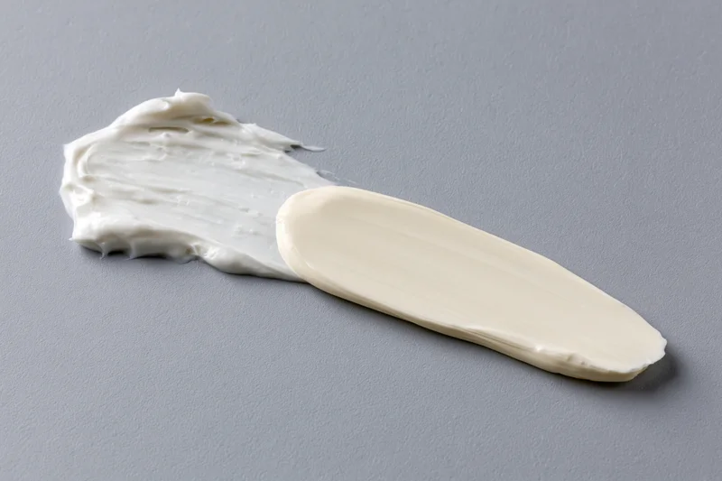 Thick white cosmetic cream smear on gray surface with plastic spatula