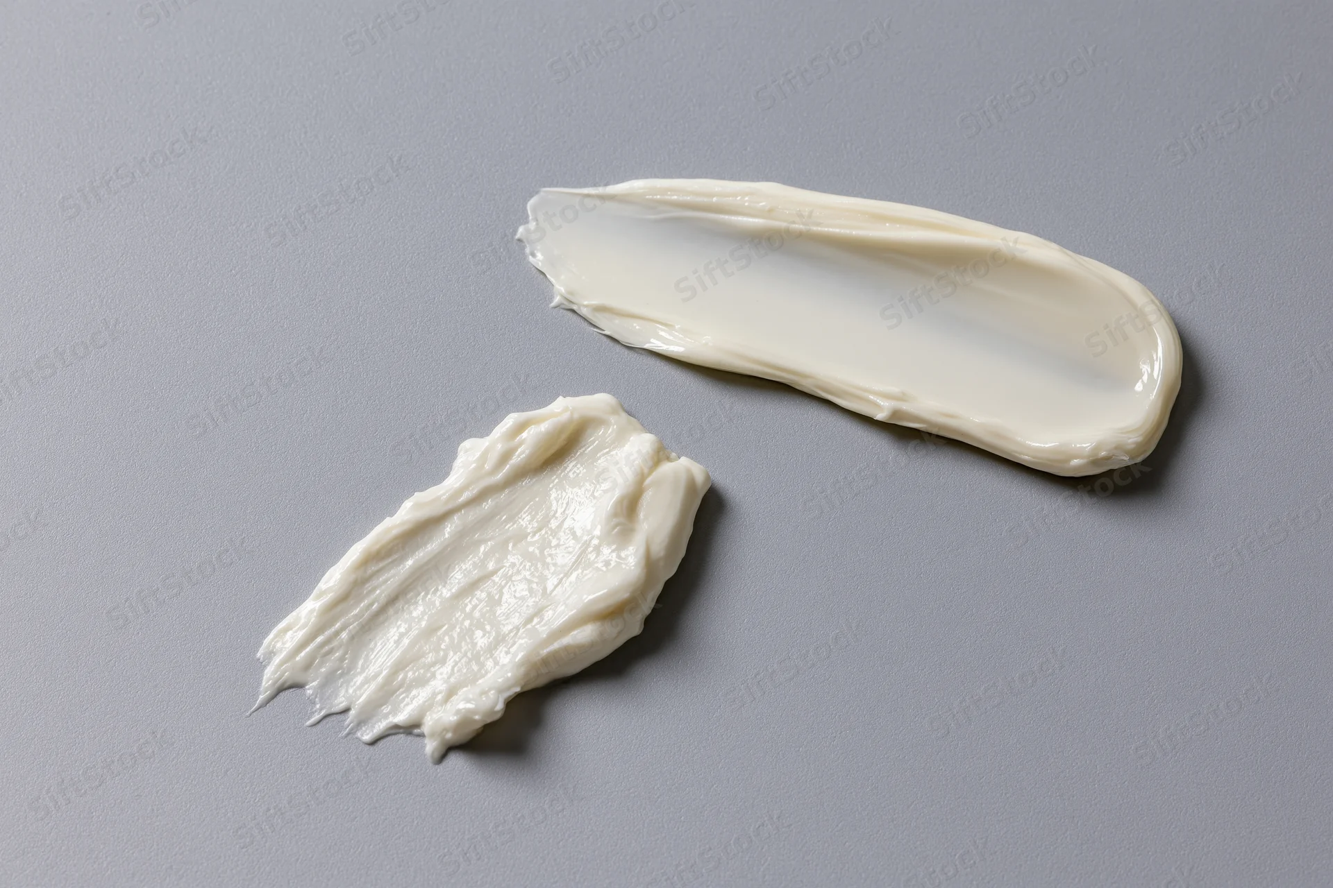 Two cosmetic cream smears on a flat surface, one thick dollop and one thin swipe, showcasing texture and consistency