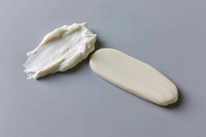Two cosmetic cream smears on a flat surface, one thick dollop and one smooth smear, isolated on gray background