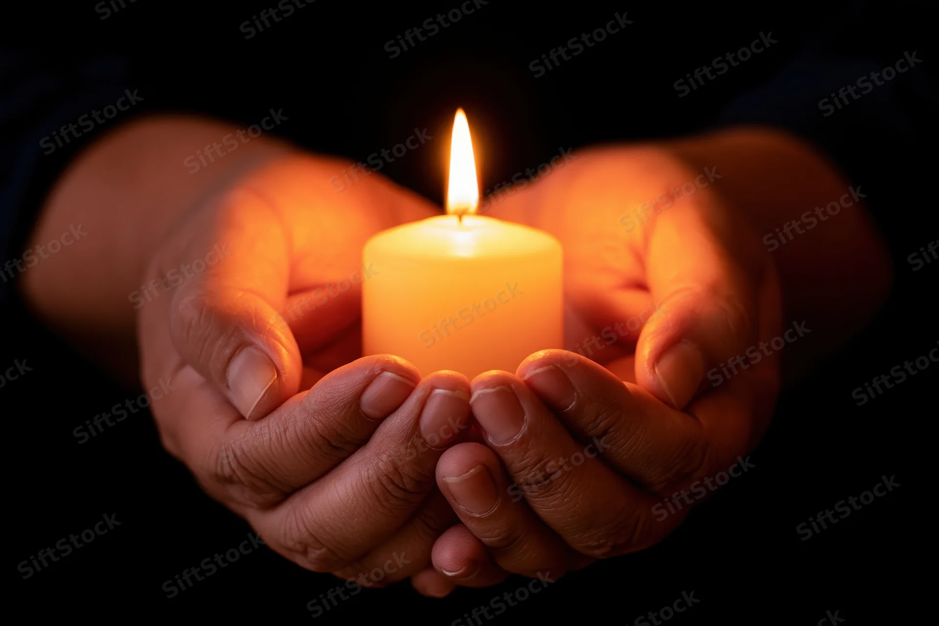 Cupped hands holding a lit candle in darkness