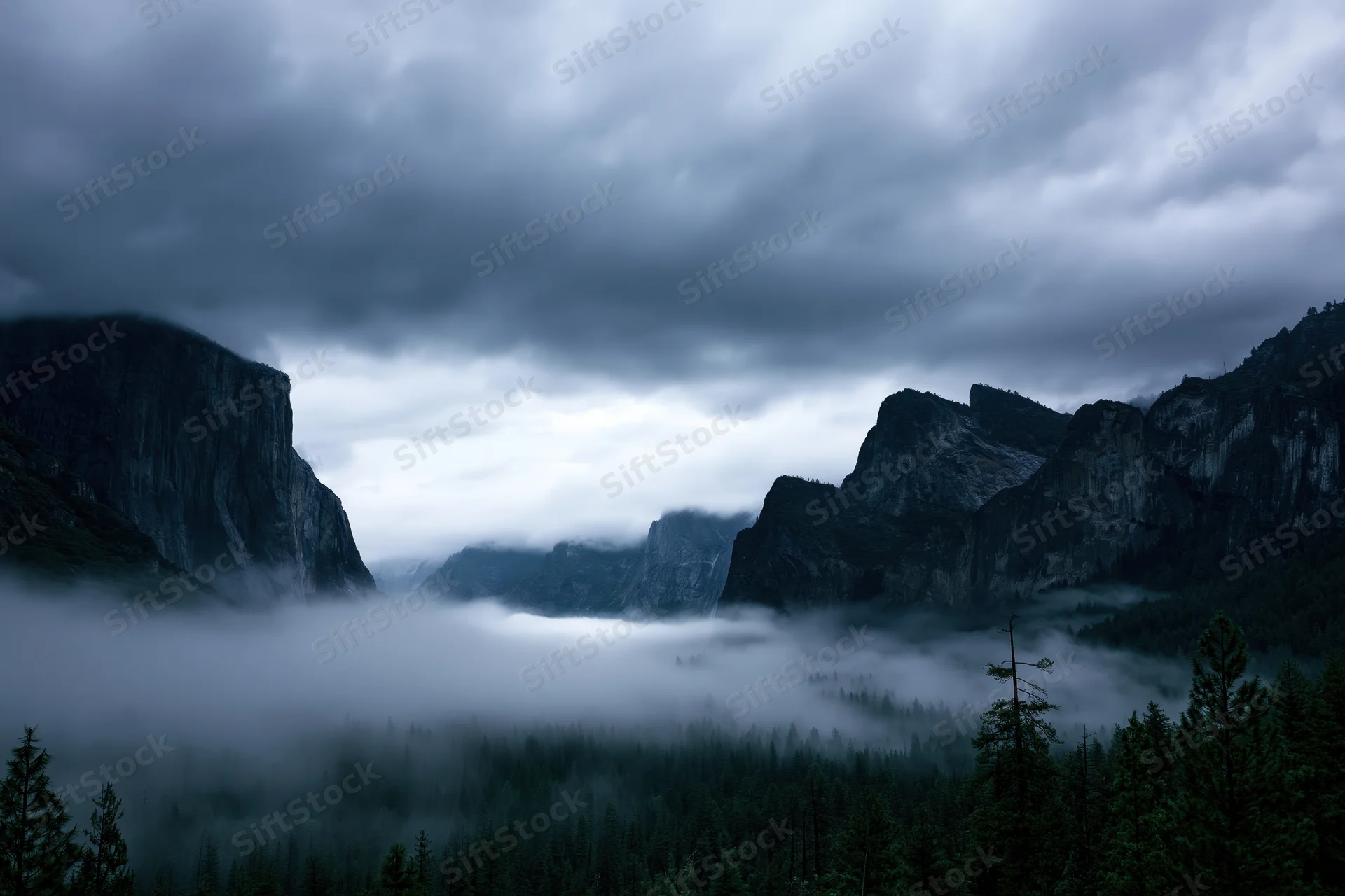 Rocky mountain peaks flanking a wide misty valley with dense forest below under cloudy sky