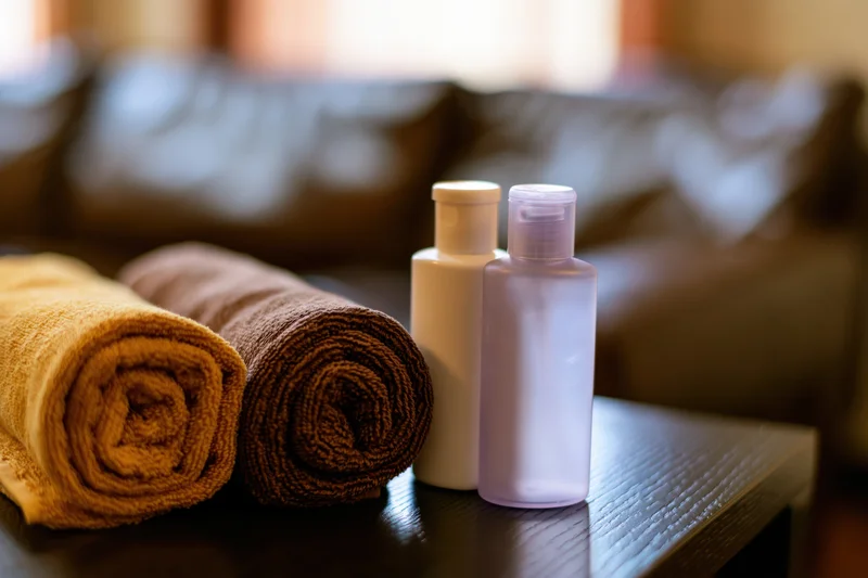 Rolled towels and toiletry bottles on a dark wooden table in a hotel room