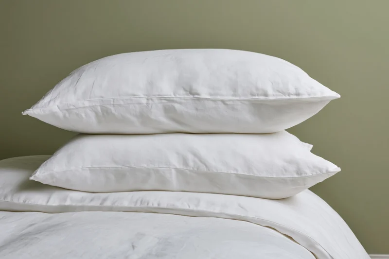Stack of white linen pillows on a neatly made bed with green wall background