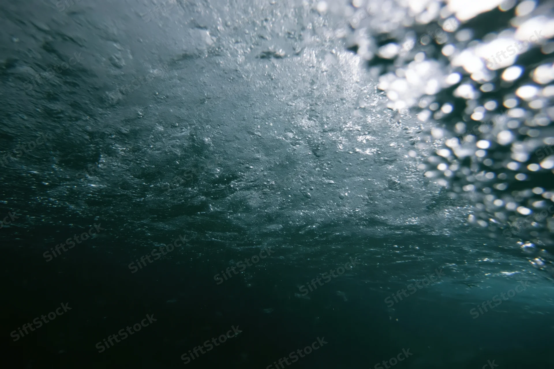View from beneath the ocean surface looking up through churning water and light reflections