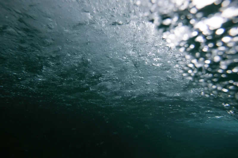 View from beneath the ocean surface looking up through churning water and light reflections