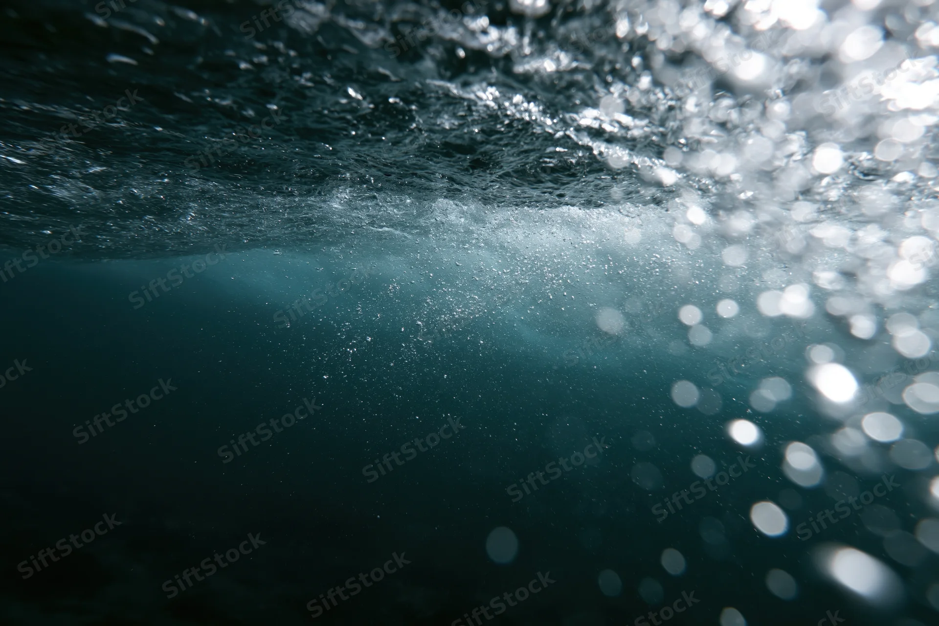 Underwater view looking up through the churning underside of a wave with sunlight filtering through bubbles and ripples