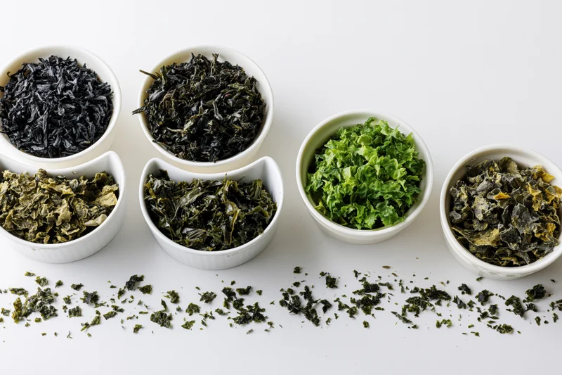 Various dried seaweed varieties in small white ceramic bowls arranged on a white surface