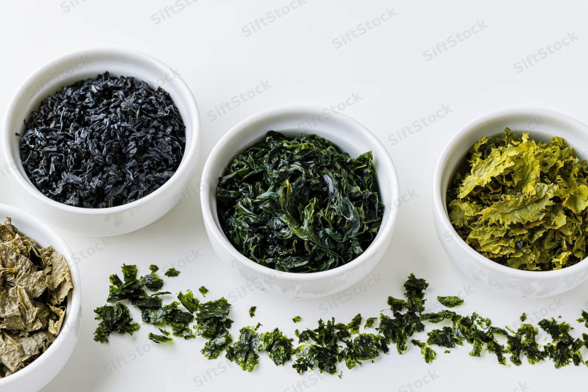 Various dried seaweed varieties in small white ceramic bowls arranged on a white surface