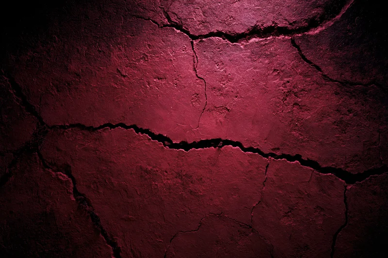 Cracked red concrete wall surface with peeling paint and deep fissures