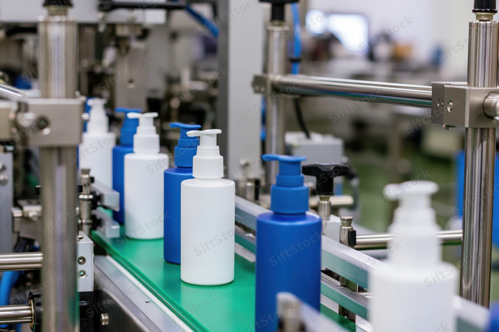 White and blue cosmetic pump bottles moving along a green conveyor in a factory