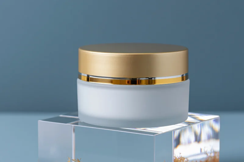 White frosted glass cosmetic cream jar with gold lid on acrylic pedestal