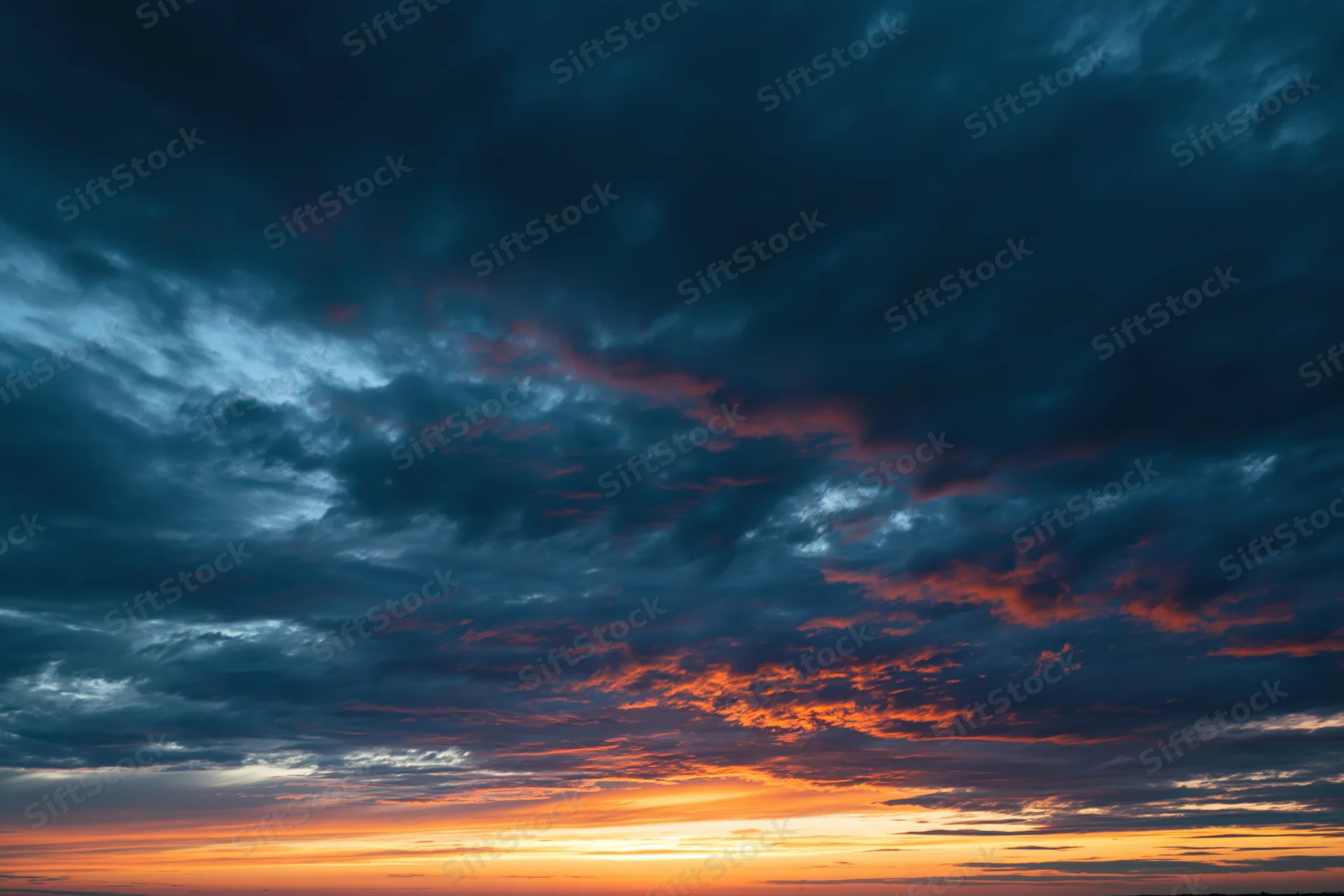 Dramatic sky at sunset with layered clouds and orange blue gradient across the horizon