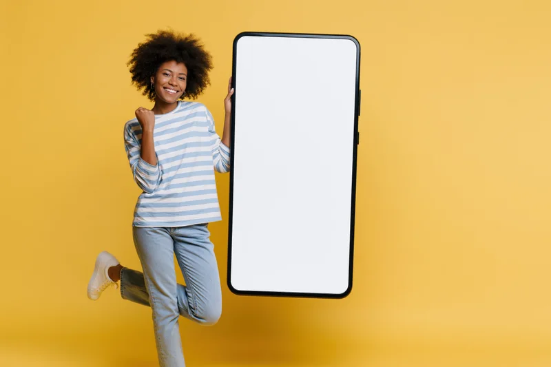 Young black woman smiling and celebrating while holding a large smartphone mockup against a yellow studio background