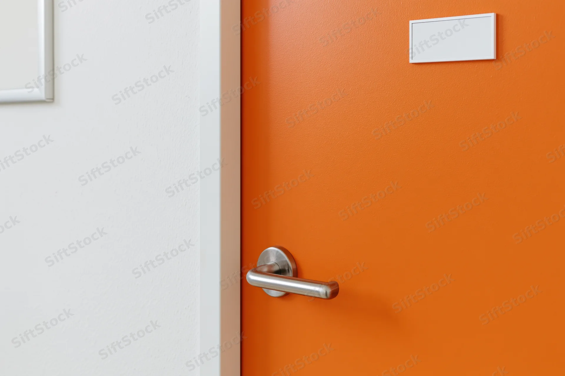 Bright orange interior door with brushed silver lever handle and blank white nameplate beside white wall
