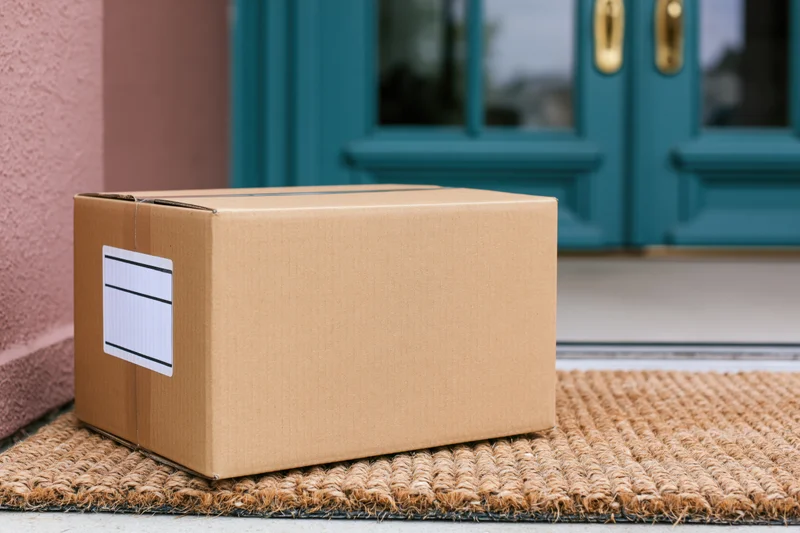Cardboard delivery box on woven doormat in front of teal front door