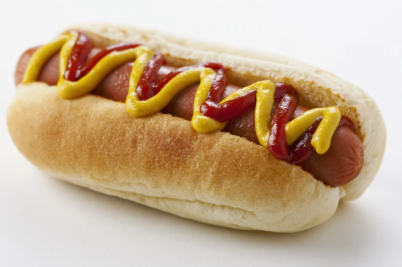 Classic hot dog in a soft white bun topped with zigzag lines of mustard and ketchup, isolated on white background