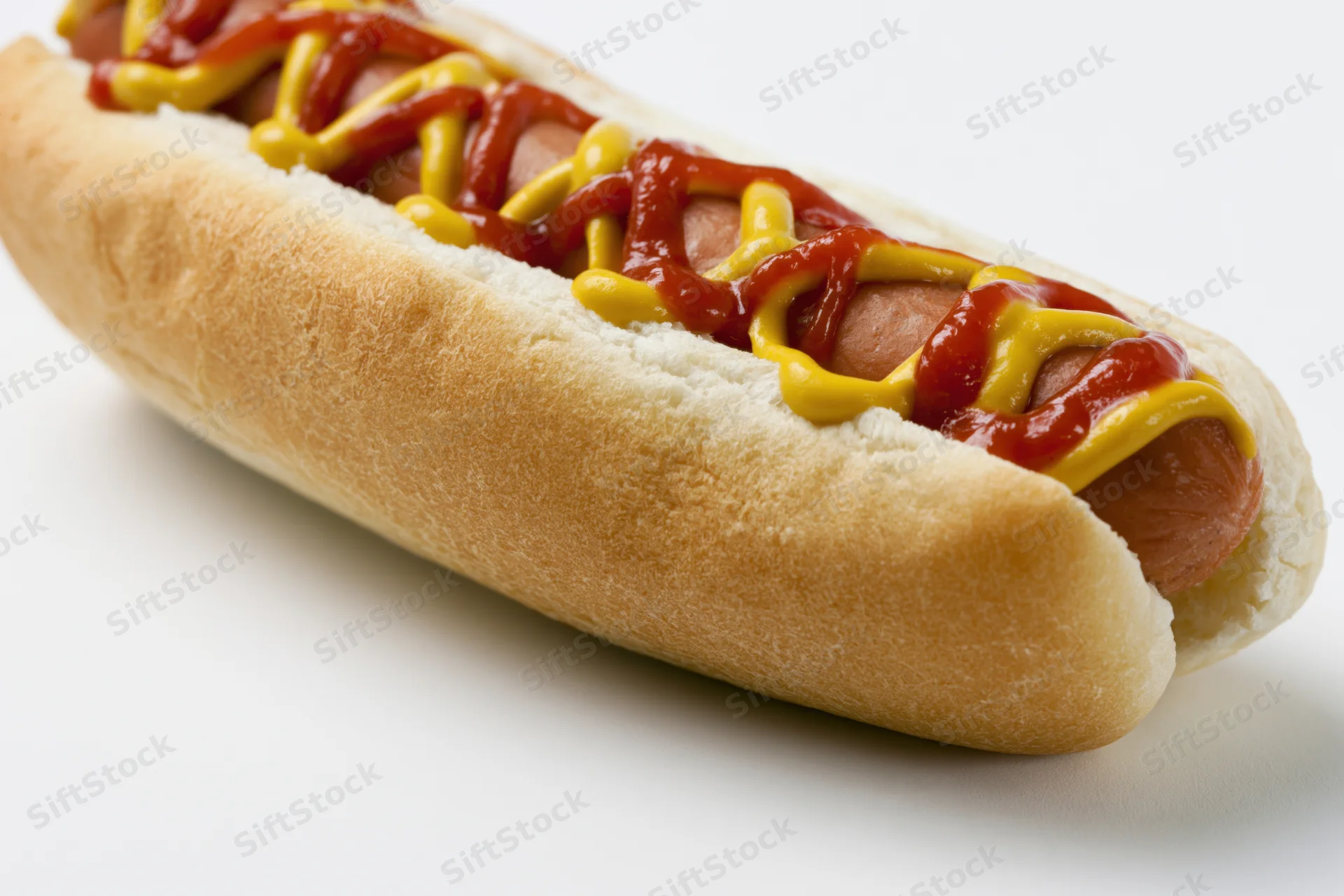 Hot dog in a soft white bun topped with zigzag ketchup and mustard lines