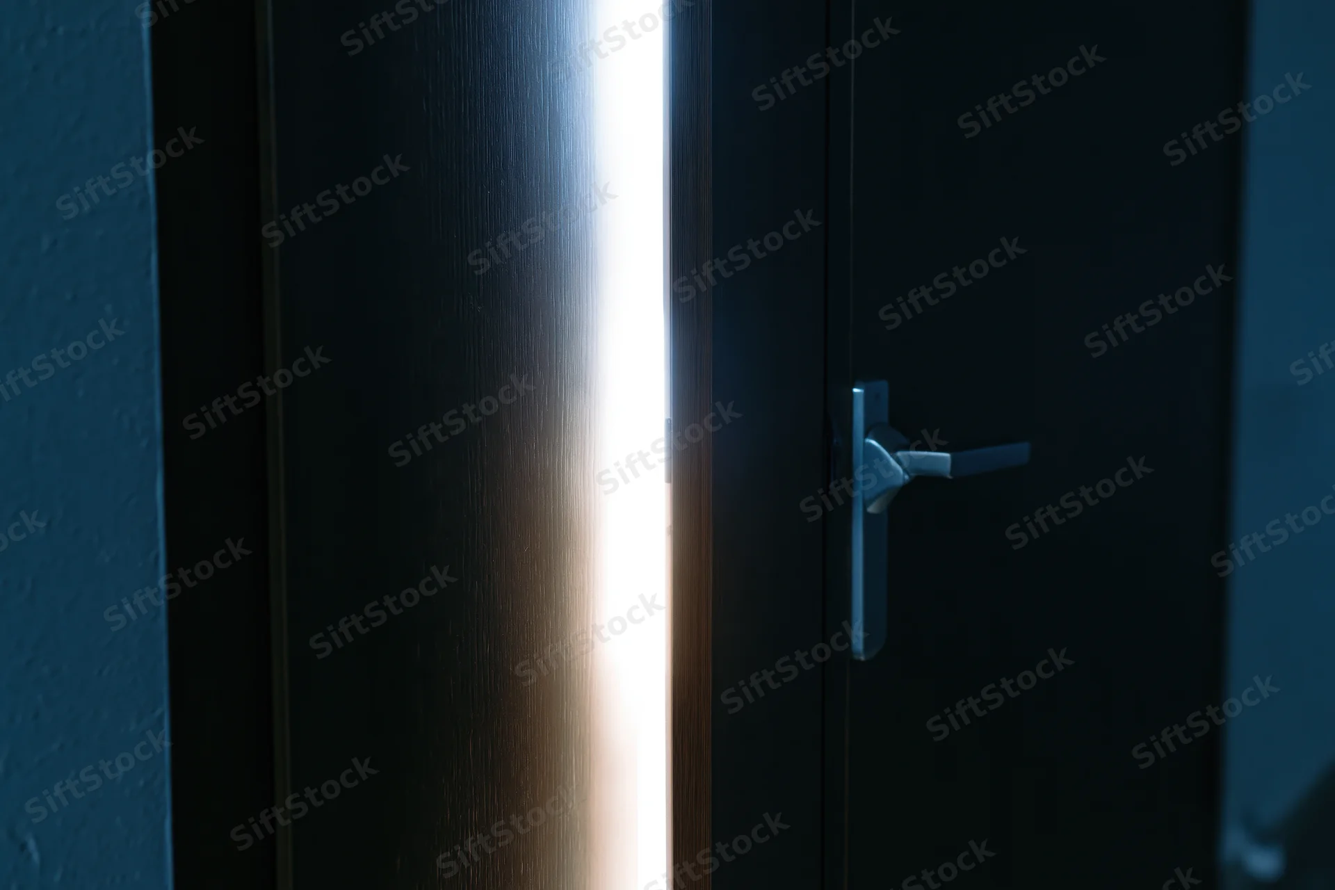 Dark wooden door slightly ajar with light streaming through the gap in a dim interior hallway