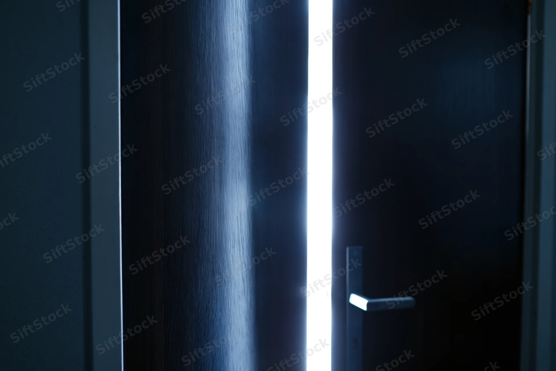 Dark wooden door slightly ajar with bright light streaming through the gap in a dim interior hallway