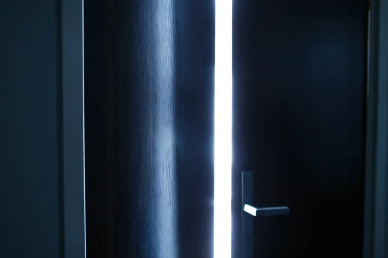 Dark wooden door slightly ajar with bright light streaming through the gap in a dim interior hallway