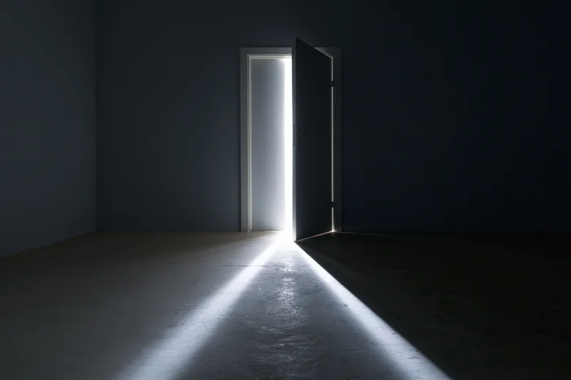 Open door in dark empty room with bright light streaming through doorway