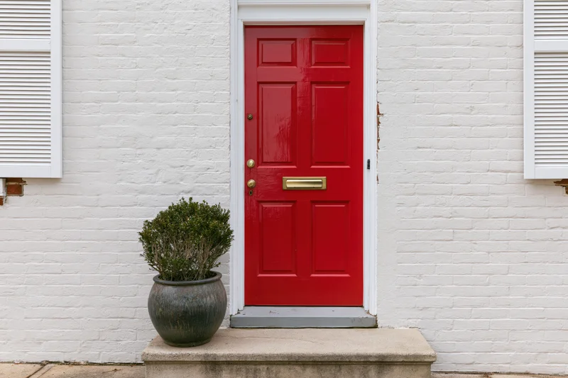 Red six-panel front door with brass hardware on white brick house exterior