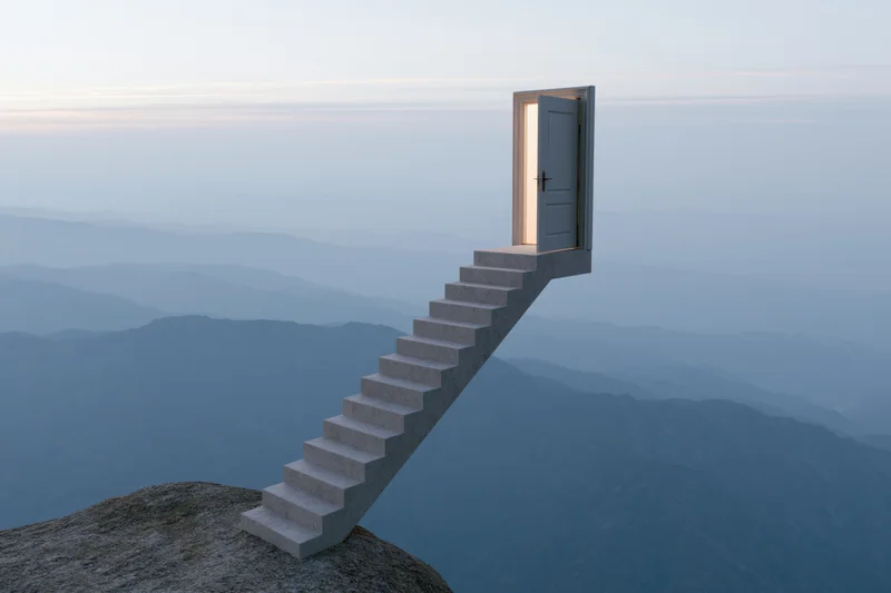 Concrete staircase rising from mountain cliff leading to open door against hazy horizon